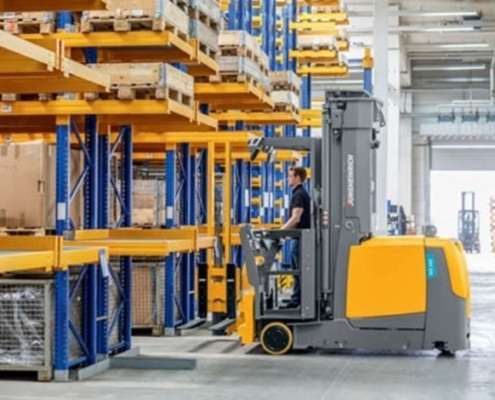 Man using forklift to go down warehouse aisle by Miami Industrial Trucks